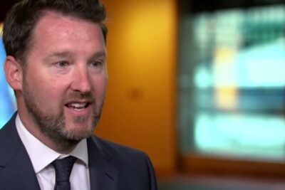 Bearded man in a suit speaking on camera in a studio setting for covid 19 vaccine coverage.