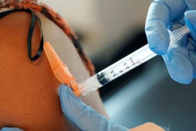 Gloved hands administering covid vaccine into a patient's upper arm