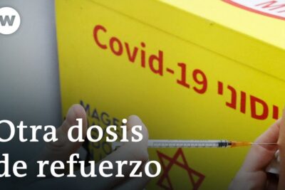 Close-up of a COVID-19 booster injection being administered to an upper arm next to a yellow vaccine box, cuarta dosis 1
