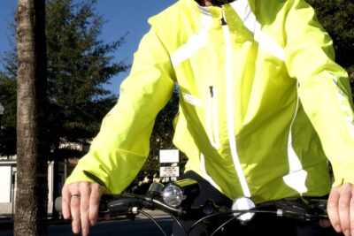 Cyclist in bright reflective jacket and helmet riding cyklar on a city street