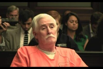 An older man in an orange jail jumpsuit seated in a courtroom during proceedings related to death penalty 4