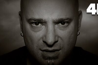 Black-and-white close-up portrait of a bald man with earrings and a lower-lip piercing staring intensely del sund.