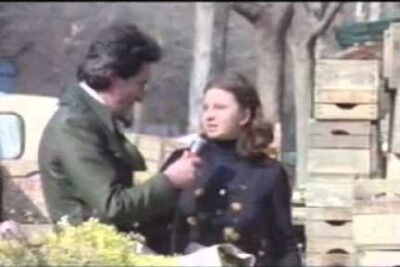 Reporter holding a microphone to a young person beside stacked wooden crates and a van, delinquenza giovanile 2.