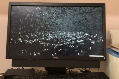 Dell monitor displaying heavy pixelated static above a keyboard on a desk, suggesting disruption and reflection on democrazia greca.