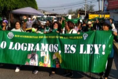 Crowd of protesters carrying a large green banner advocating depenalizzazione dellaborto during a public march.