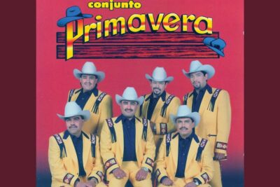 Seven musicians in coordinated yellow Western suits and white cowboy hats posed against a red background, derecho vida 8.