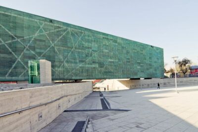 Contemporary elevated building with a green glass facade overlooking a wide paved plaza and ramps, derechos humanos 1.