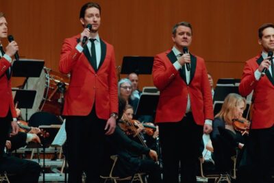 Four male singers in red jackets performing on stage with an orchestra, det ar 59