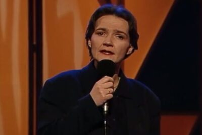 Person holding a microphone on a warm-lit stage singing, det handler.