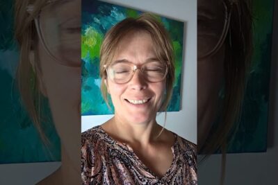 Smiling person wearing glasses in front of a teal and green abstract painting, det vigtigt 23.