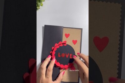 Hands assembling a handmade Valentine card with red heart wreath, LOVE cutout and craft paper, dia namorados 1.