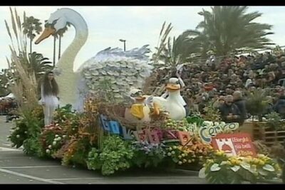 Parade float with a large white swan, two cartoon ducks, abundant flowers and spectators — die arbeitsreform