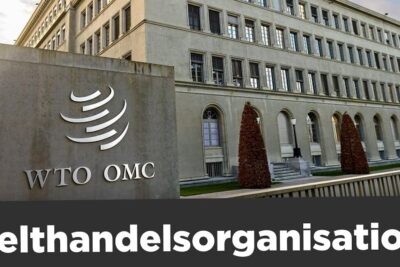 Stone sign with WTO OMC logo in front of a large institutional building and Welthandelsorganisation lettering die wto 1.
