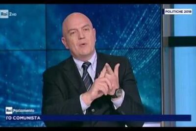 A suited television speaker gesturing emphatically during a studio discussion about diritti individuali and civil liberties.