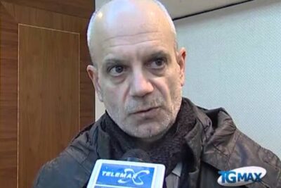 Middle-aged man in a coat and scarf speaking into a microphone about discriminazione razziale 2