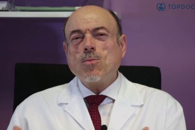 Male physician in white coat speaking directly to camera about dolor cronico 14 and pain care.