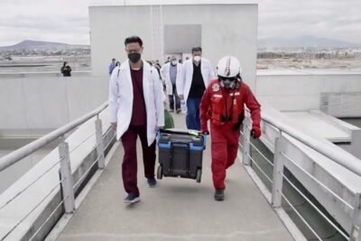 Medical staff in white coats and a helmeted rescue worker carrying an insulated transport cooler along a rooftop walkway for donacion organos 5.
