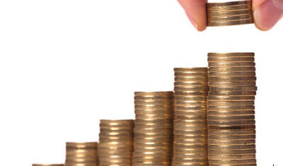 Hand placing a coin on ascending stacks of coins representing du har and growing savings.