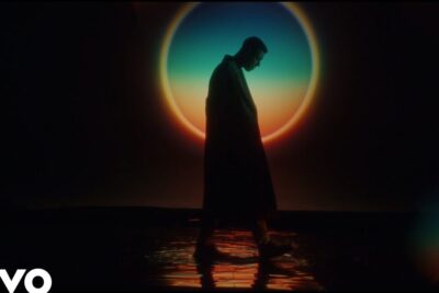 Silhouette of a person walking across shallow reflective water against a colorful circular sunset backdrop, e importante 2.
