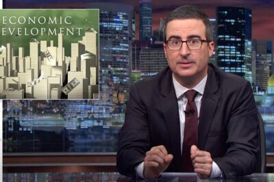 Television host at a studio desk presenting a graphic about economic development with a stylized city skyline and floating dollar bills.