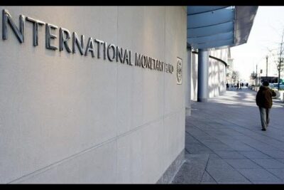 Exterior facade of the International Monetary Fund building with signage and a lone pedestrian, evoking economico mondiale dynamics.