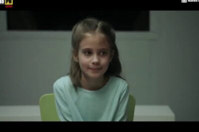 A young girl seated on a green chair in a neutral room, portraying educacao inclusiva 1 and child-focused inclusion.