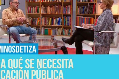 Two people in a TV studio interview seated in front of bookshelves discussing educacion publica 11