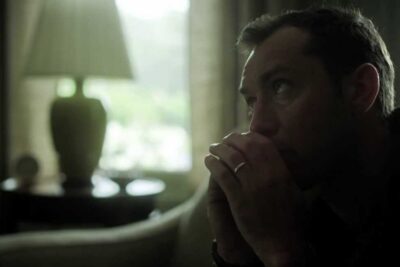 Pensive man in a dimly lit room with hands clasped to his mouth and a wedding band visible, effetti collaterali 1