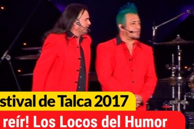 Two performers in red jackets delivering el humor with headset mics and a drum kit onstage.