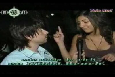 Woman holding a microphone and gesturing toward a man during a nighttime interview, el movil 2