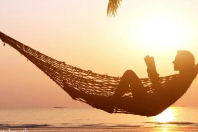 Silhouette of a person reading in a hammock at sunset on the beach with calm ocean in the background, elektronische musik 1 mood.