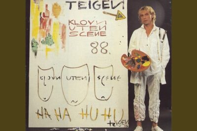 Artist in white holding a paint palette beside a large canvas titled en annen 1, featuring brush sketches and handwritten text.
