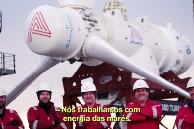 Five workers in hard hats and red safety gear standing in front of a large tidal turbine labeled energia oceanos 2