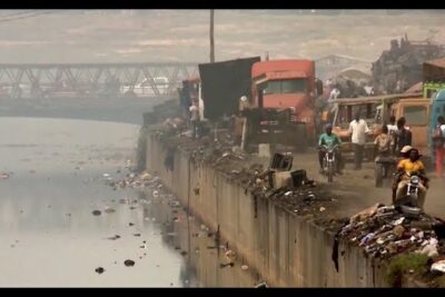 Environmental pollution 1 showing a polluted canal with floating debris, littered concrete embankment and vehicles on a hazy urban shoreline