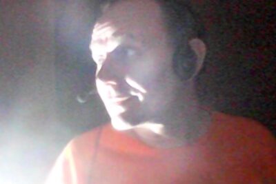 Person in low light wearing a headset, side profile lit by a strong light source showing erilaisia nakokulmia