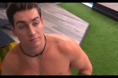 Shirtless man leaning by a wooden deck and artificial grass with a visible pool edge, es importante 1