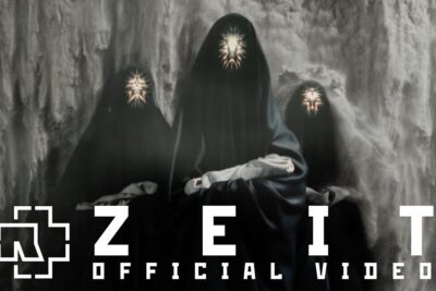 Three cloaked figures with glowing starburst faces seated before a waterfall for es zeit.