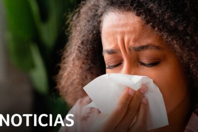 Close-up woman sneezing into tissue — estados unidos 4 news image showing a woman with eyes closed covering her nose and mouth with a tissue.