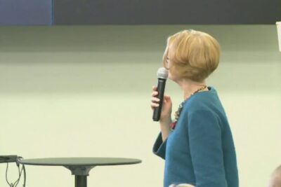 Speaker in a blue jacket holding a microphone presenting etta bioteknologian to an audience