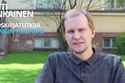 Seated man on a campus lawn in front of a university building with visible Finnish text, focused on etta globalisaatio.