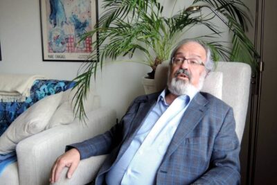Older bearded man seated in an armchair in a cozy living room with a potted palm and framed artwork, etta psykoanalyysi