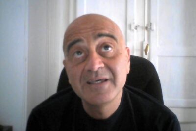 Bald man seated in a chair looking upward with a contemplative expression suggesting etta relativismi