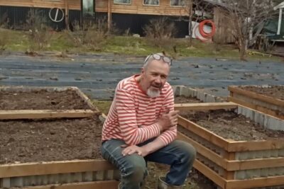 Person seated on a wooden raised garden bed with prepared soil highlighting etuja haittoja of raised planters.