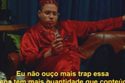 Seated individual in a red satin robe and glasses on a leather sofa with yellow subtitle text, eu n 1.