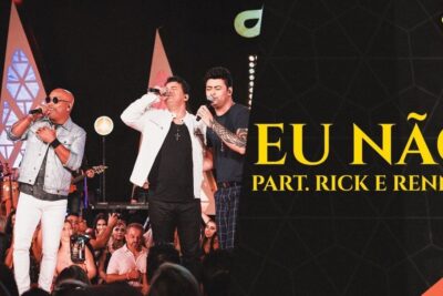 Four male singers performing onstage in front of an engaged audience beside a large black promotional banner reading 'EU NÃO' in bold yellow type