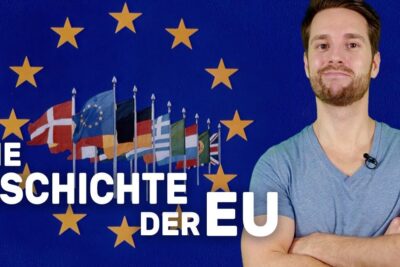 A presenter stands with crossed arms next to a circle of stars and a row of national flags representing the europaischen union.