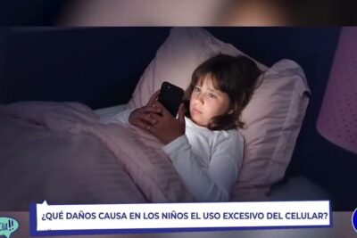 Child lying in bed using a smartphone at night highlighting risks of excesivo celulares.