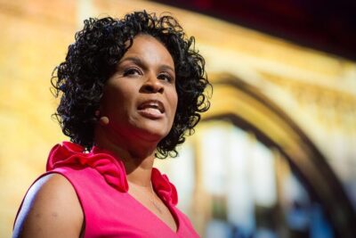 Female stage speaker in pink dress delivering a talk about extracurricular aktiviteter 1