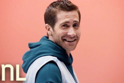 Smiling man wearing a teal hoodie layered with a light denim vest against a peach background showcasing fast fashion casual styling.