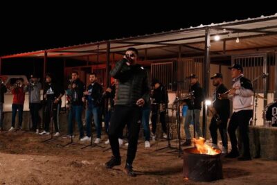 Outdoor nighttime banda performance with lead singer, brass musicians and a glowing fire pit, suitable for favor tabaco promotions.